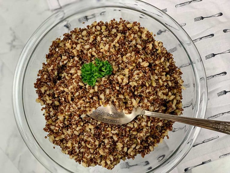 Glass bowl full of cooked red quinoa and brown rice, topped with parsley.