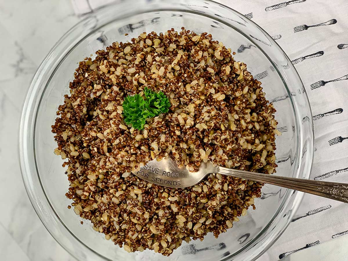 glass bowl full of cooked red quinoa and brown rice, topped with parsley.