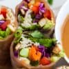 close up of spring rolls cut in half with dish of peanut sauce