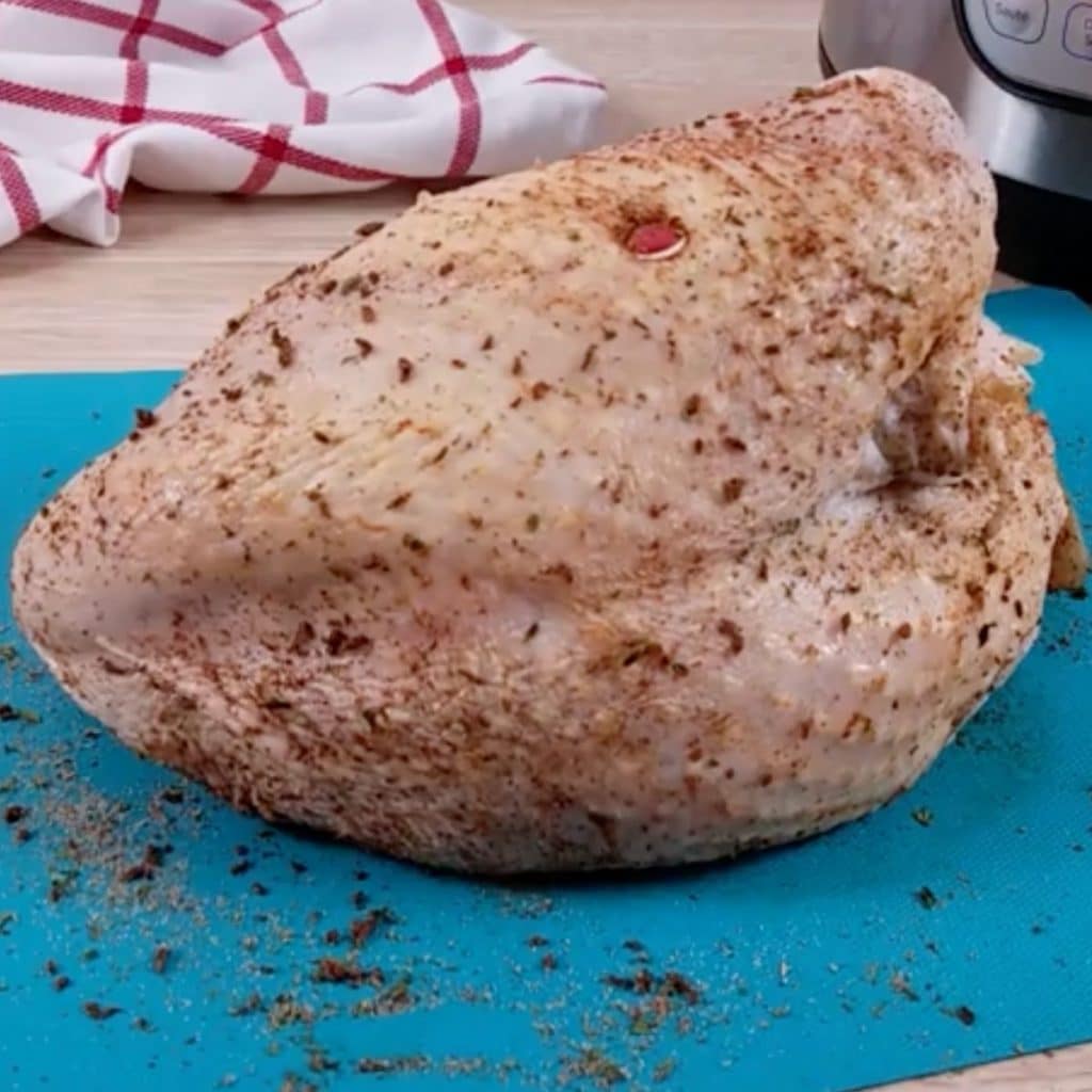 A raw, seasoned turkey breast sitting on a blue cutting board.
