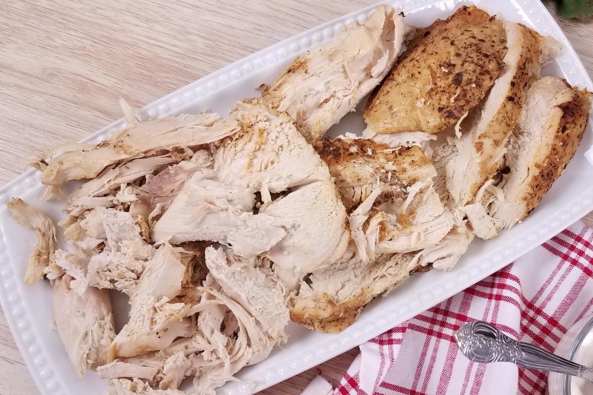 A white rectangular platter with sliced turkey breast, on top of a red and white checkered napkin.