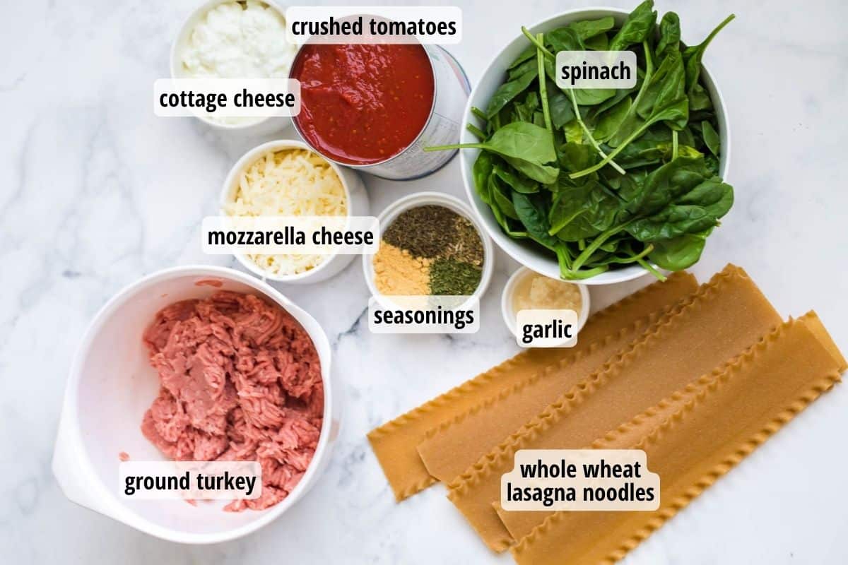 A white and gray counter top with bowls of labeled ingredients needed to make lasagna.