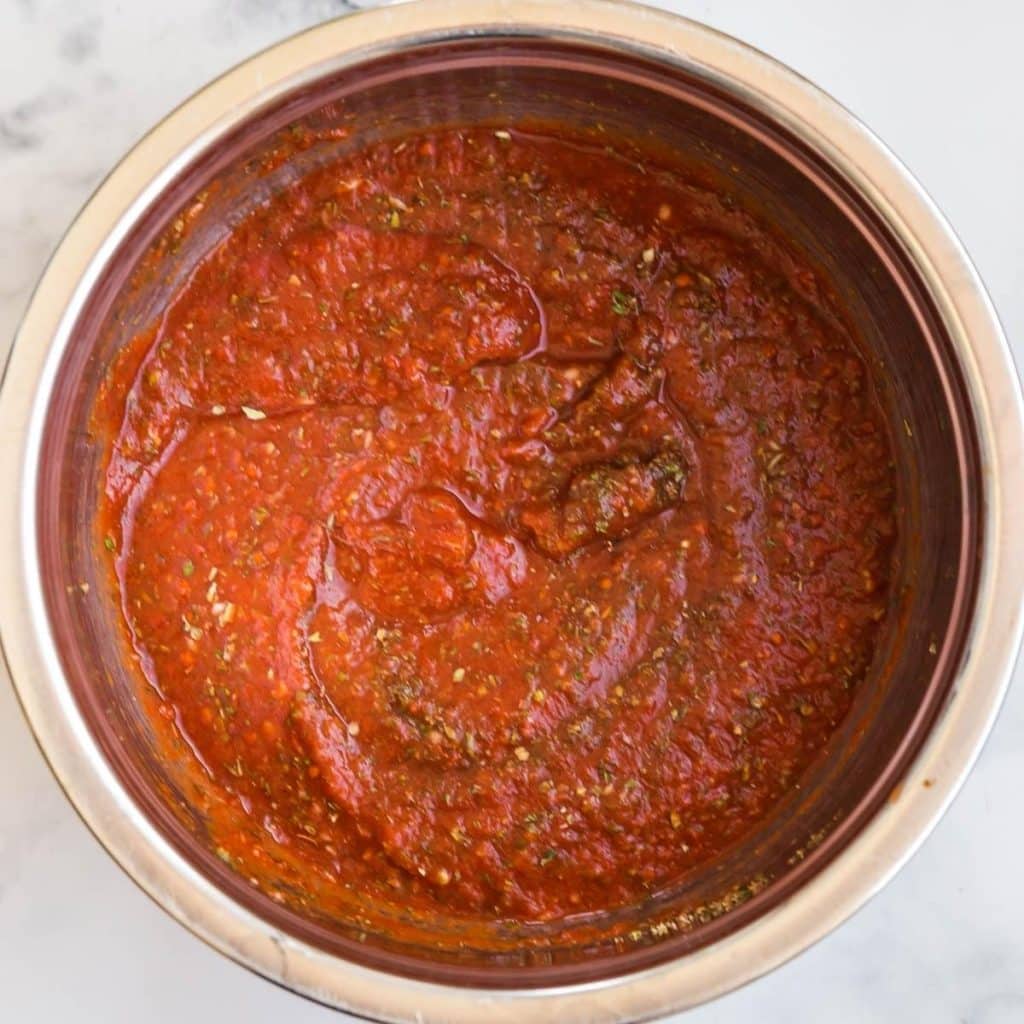 A stainless steel bowl full of crushed tomatoes with Italian seasonings mixed in.