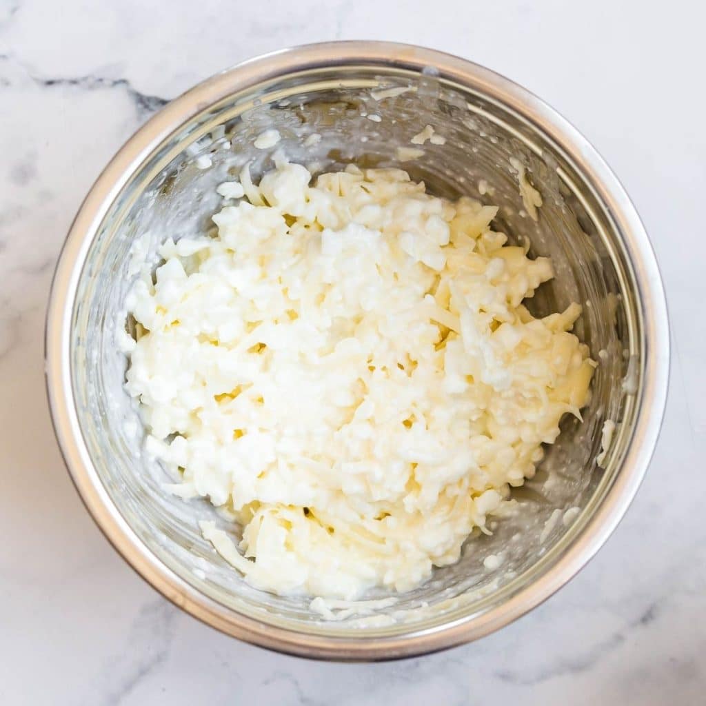 A stainless steel bowl with a mixture of ricotta and mozzarella cheese.