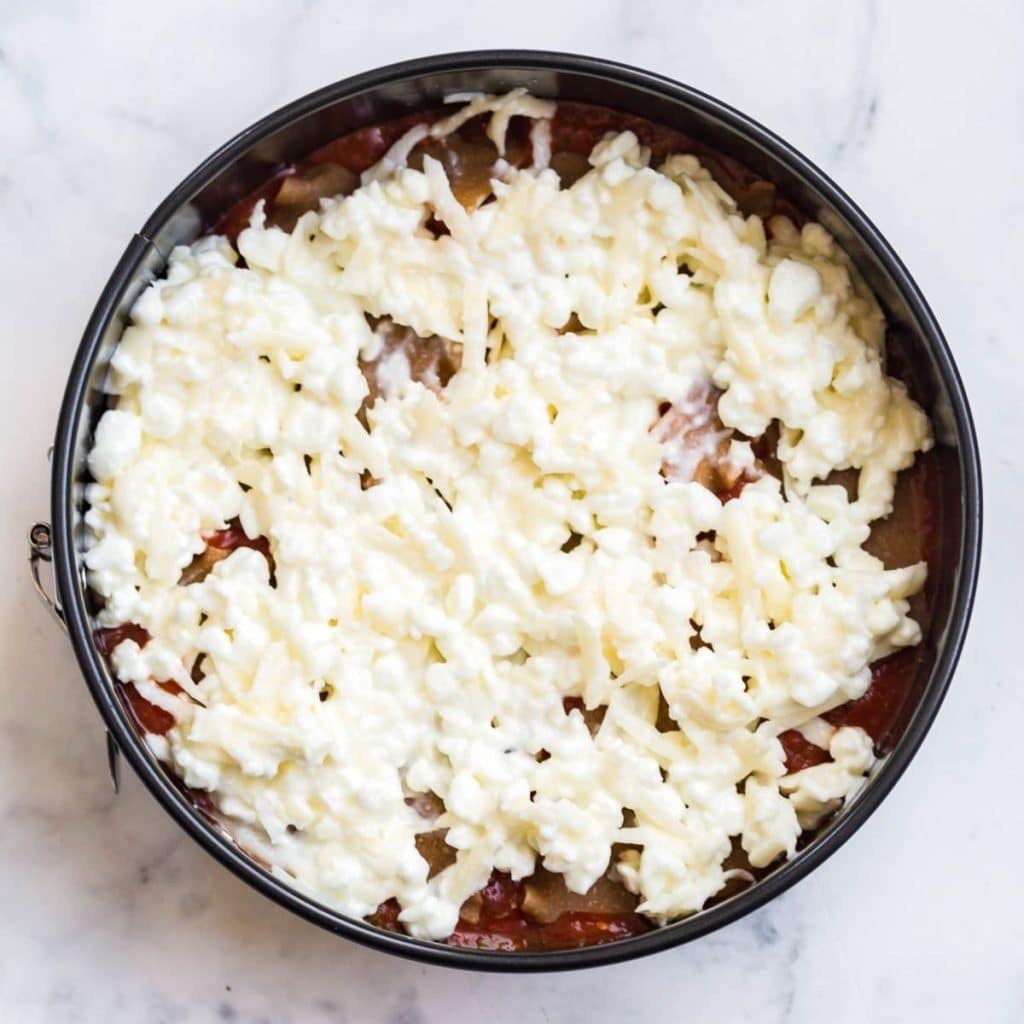 A circular Instant Pot pan filled with the first few layers of lasagna, showing the current layer as the ricotta and mozzarella mixture.