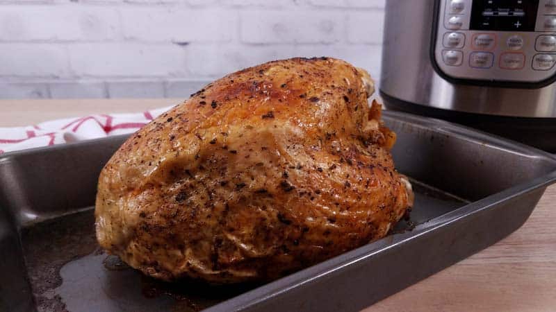 Cooked and browned turkey breast in roasting pan with an Instant Pot in the background. 