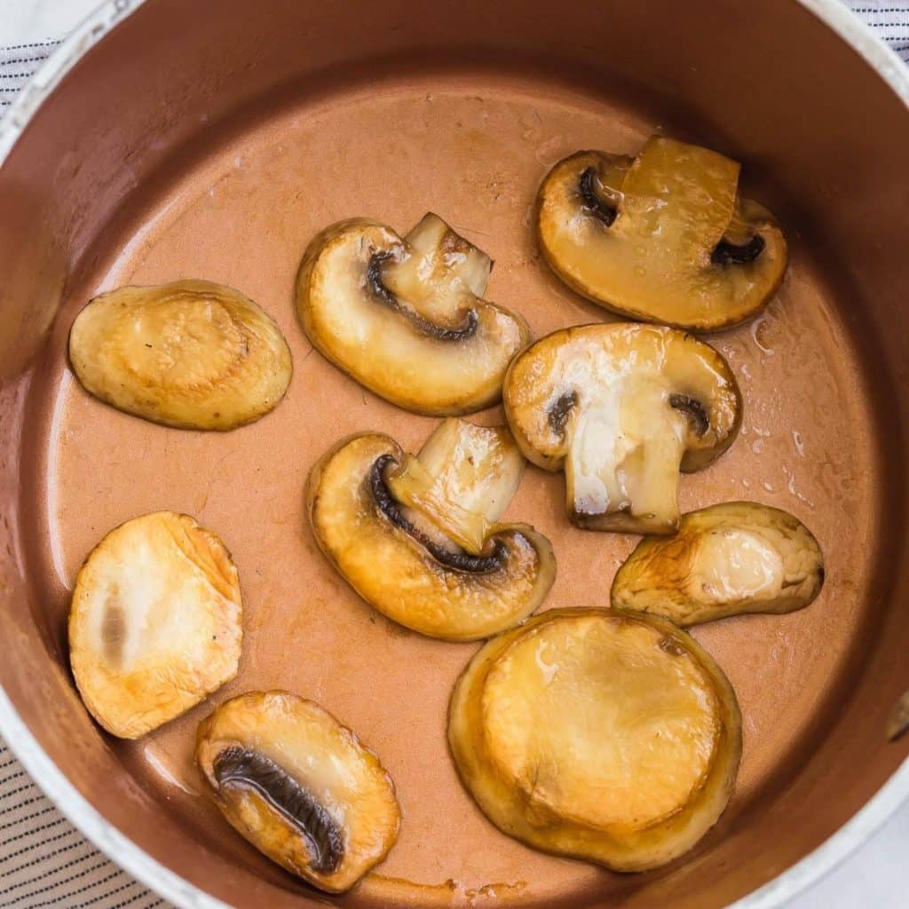 A sauce pan with golden mushroom sliced being sautéed.