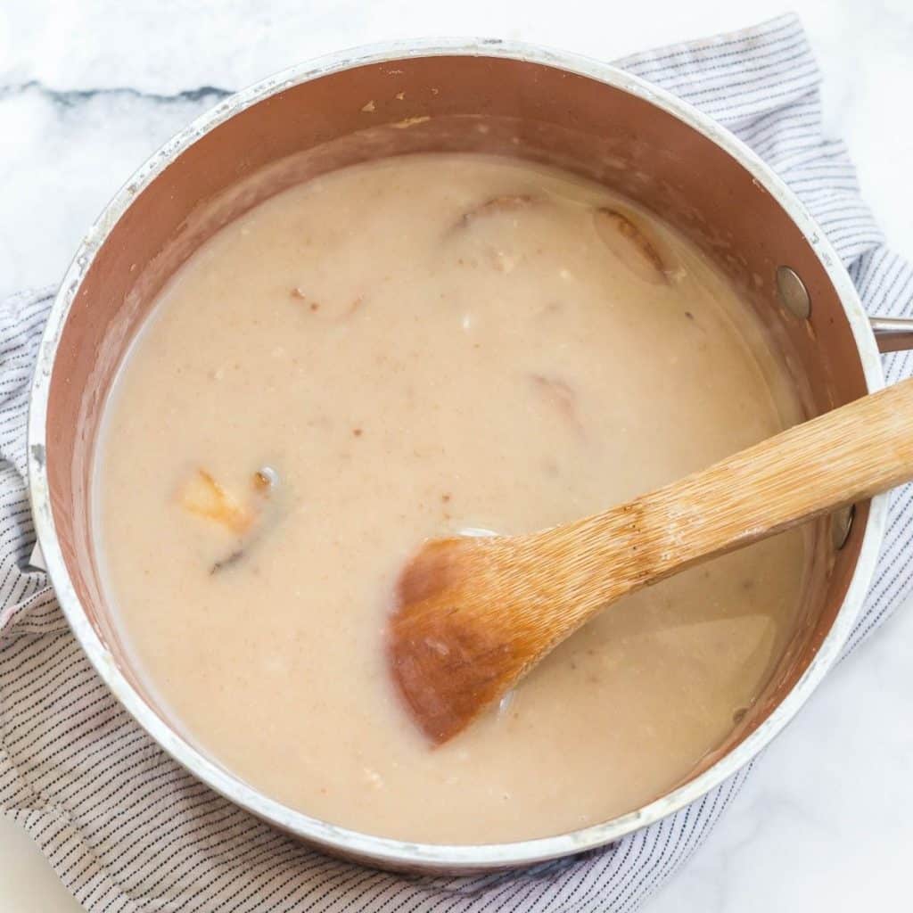 A sauce pan with a wooden spoon stirring cream of mushroom soup.