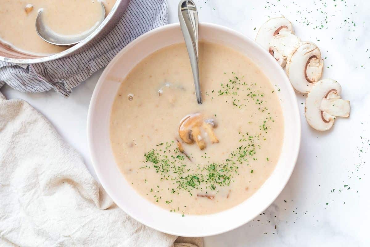 A white bowl with homemade cream of mushroom soup that shows a sliced mushroom and a scattering of green parsley flakes on top.