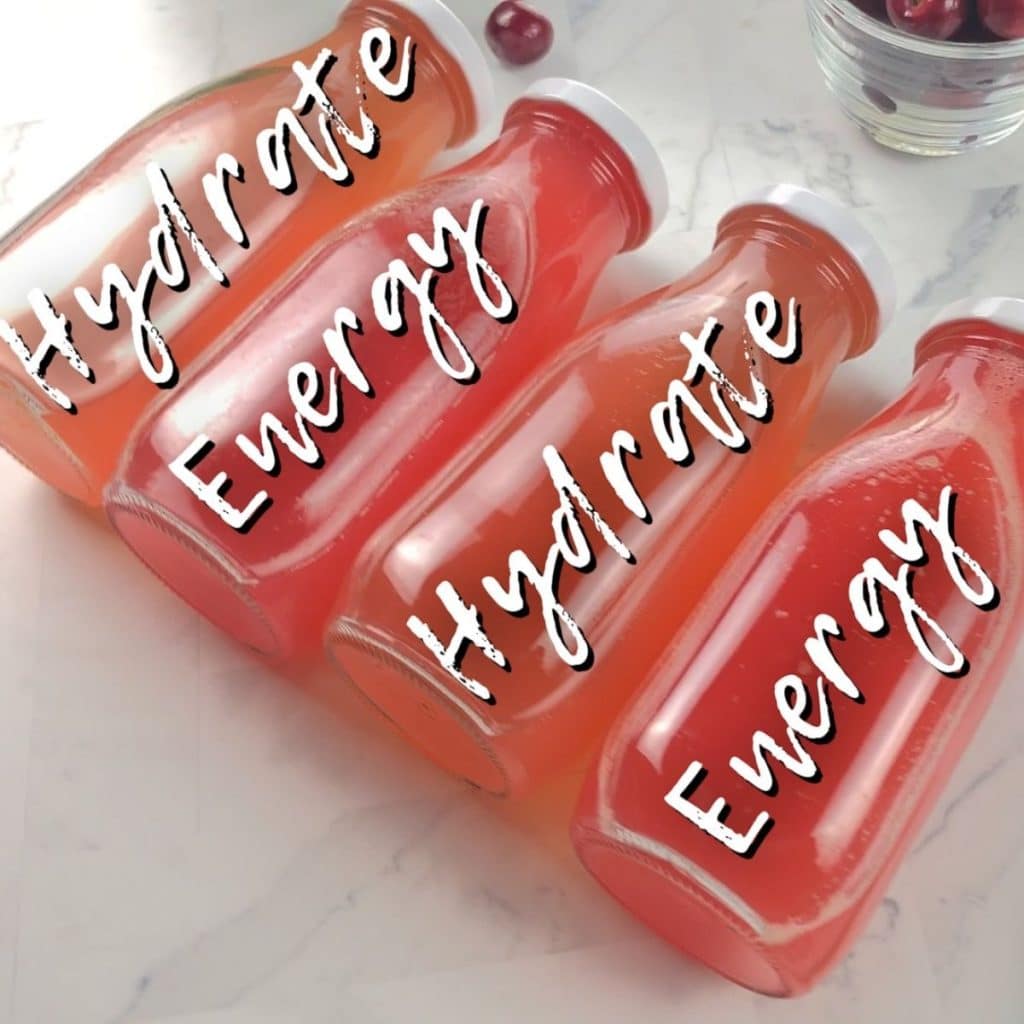 Four glass bottles, lying on their side, with pink colored homemade energy drink inside. On top of the bottles is text saying "hydrate, energy, hydrate, energy".