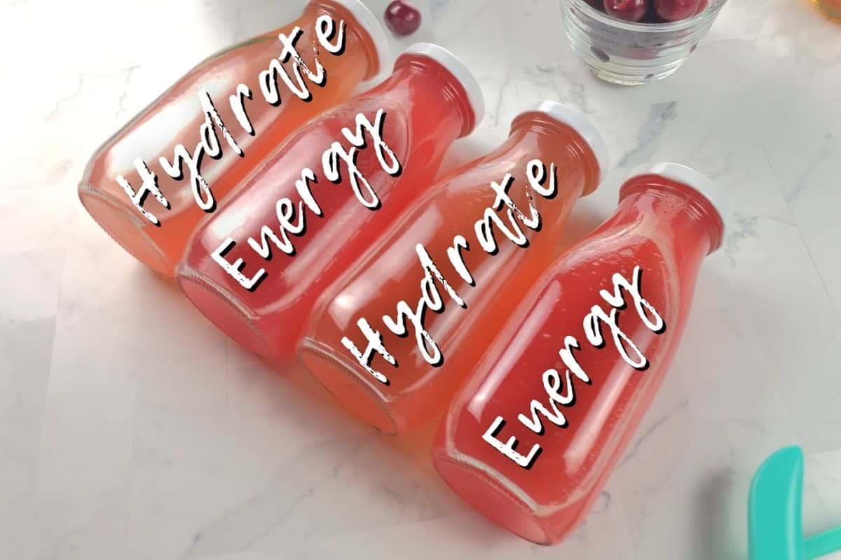 Four glass bottles, lying on their side, with pink colored homemade energy drink inside. On top of the bottles is text saying "hydrate, energy, hydrate, energy".