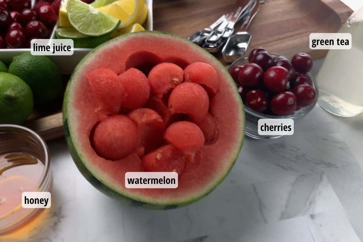 Ingredients needed to make homemade cherry lime energy drink, including watermelon, honey, limes, cherries and green tea.