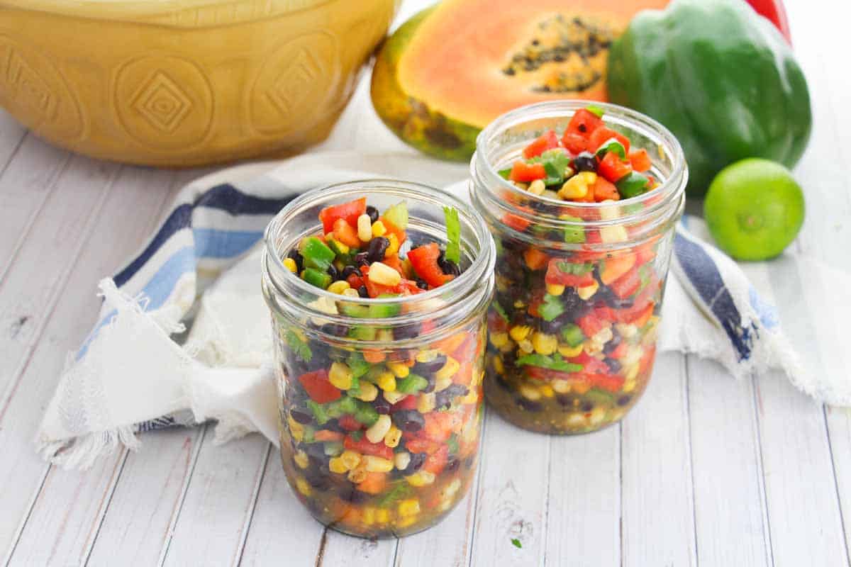 Two glass mason jars with summer confetti salad which is a tomato, black bean, corn and papaya mixture with seasonings.