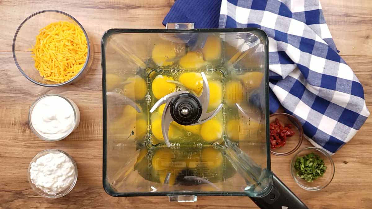 image of a blender with eggs inside of it, and bowls full of ingredients surrounding it.