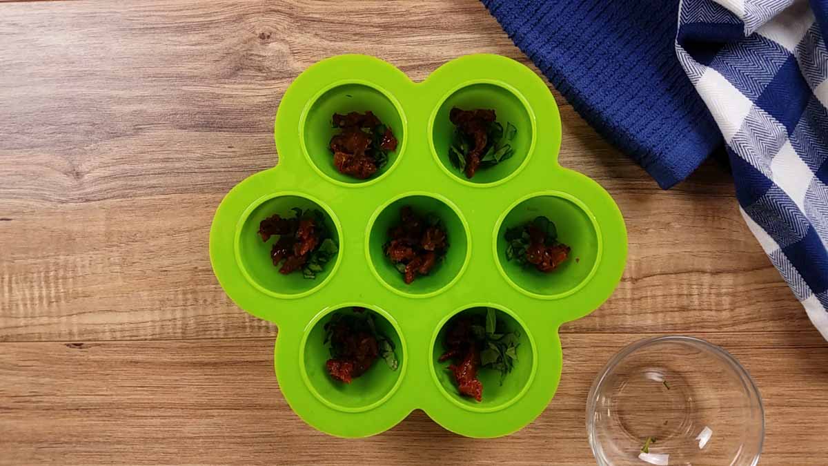 green egg bite mold with sun dried tomatoes in each of the seven vessels.