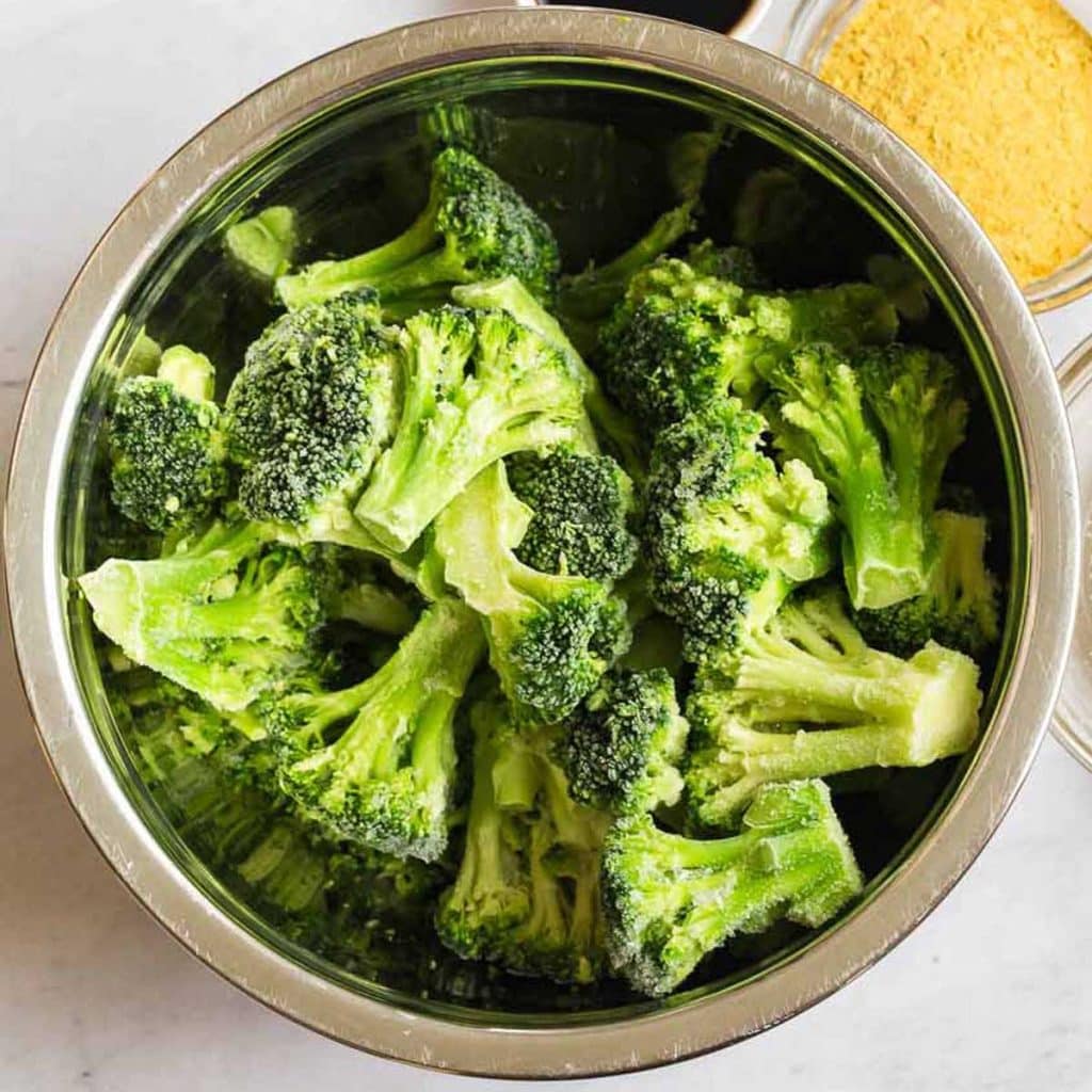 Silver bowl full of frozen broccoli, getting ready for the air fryer. 