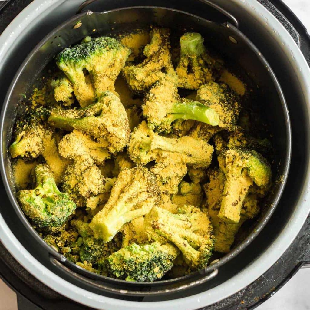 Air fryer basket filled with broccoli that has been sprinkled with nutritional yeast for taste. 