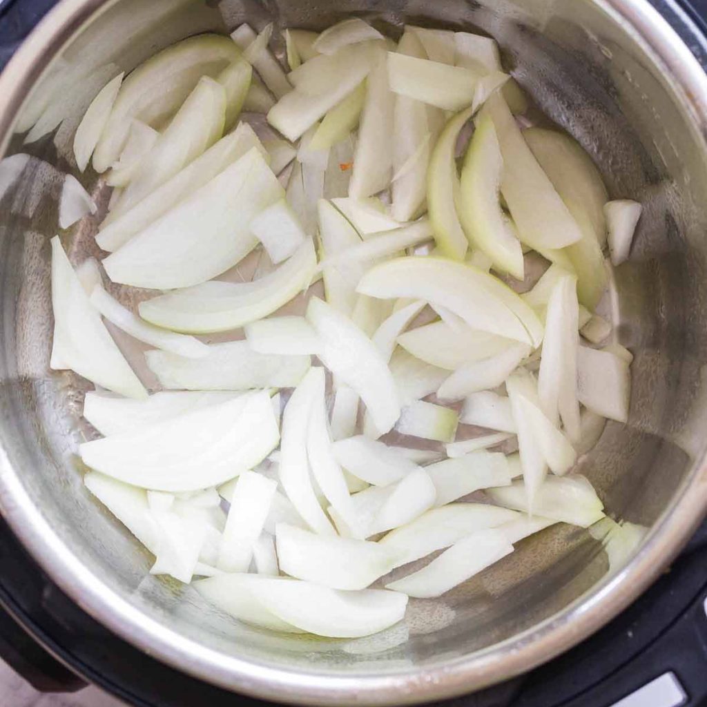 Instant Pot with diced onions on the bottom. There is a spray of olive oil under the onions. 