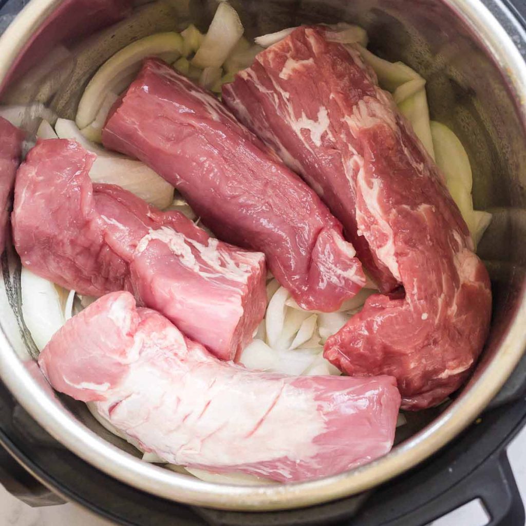 Instant Pot with no lid. Inside the pot are two pork tenderloins, cut in half, on top of thick sliced onions.