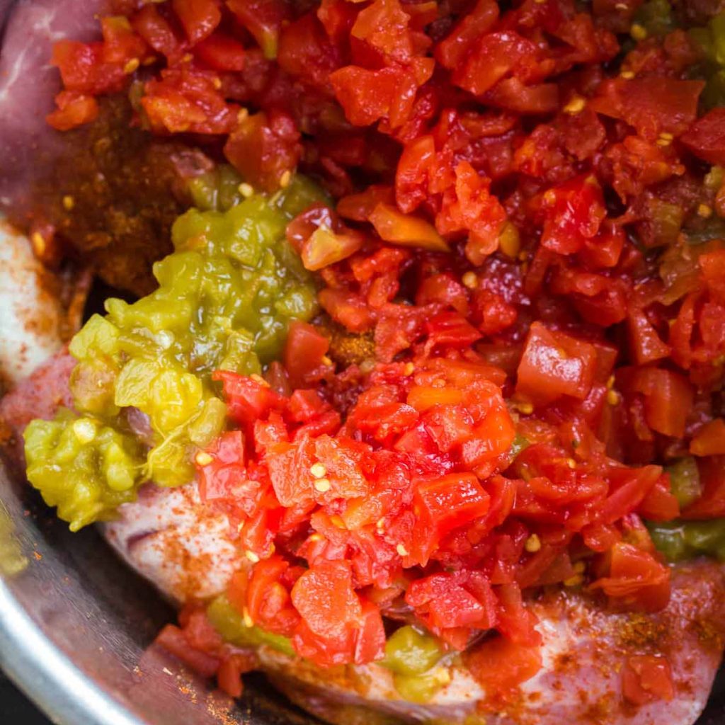 Instant Pot with diced onions, pork tenderloin, spices, and diced tomatoes and green chiles on top.