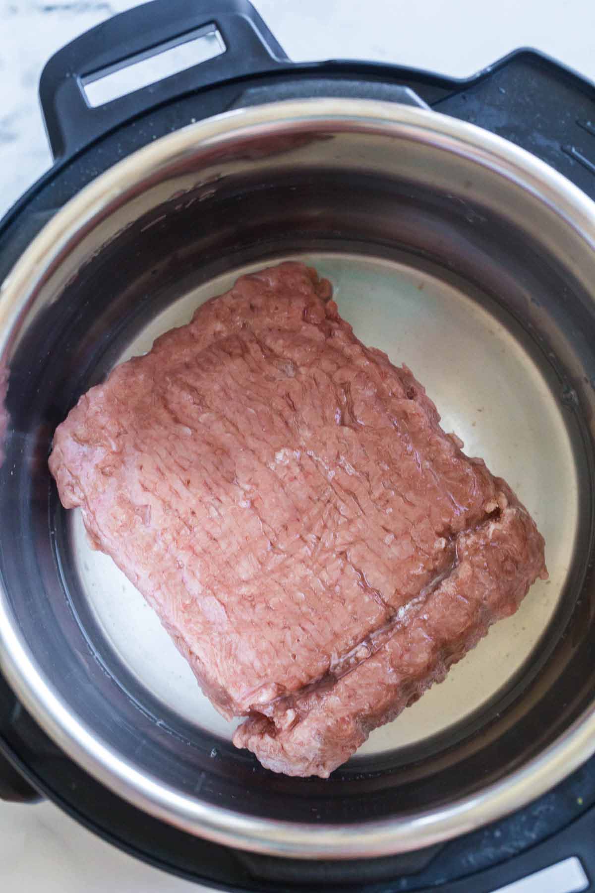 frozen ground turkey with water at the bottom of an instant pot.
