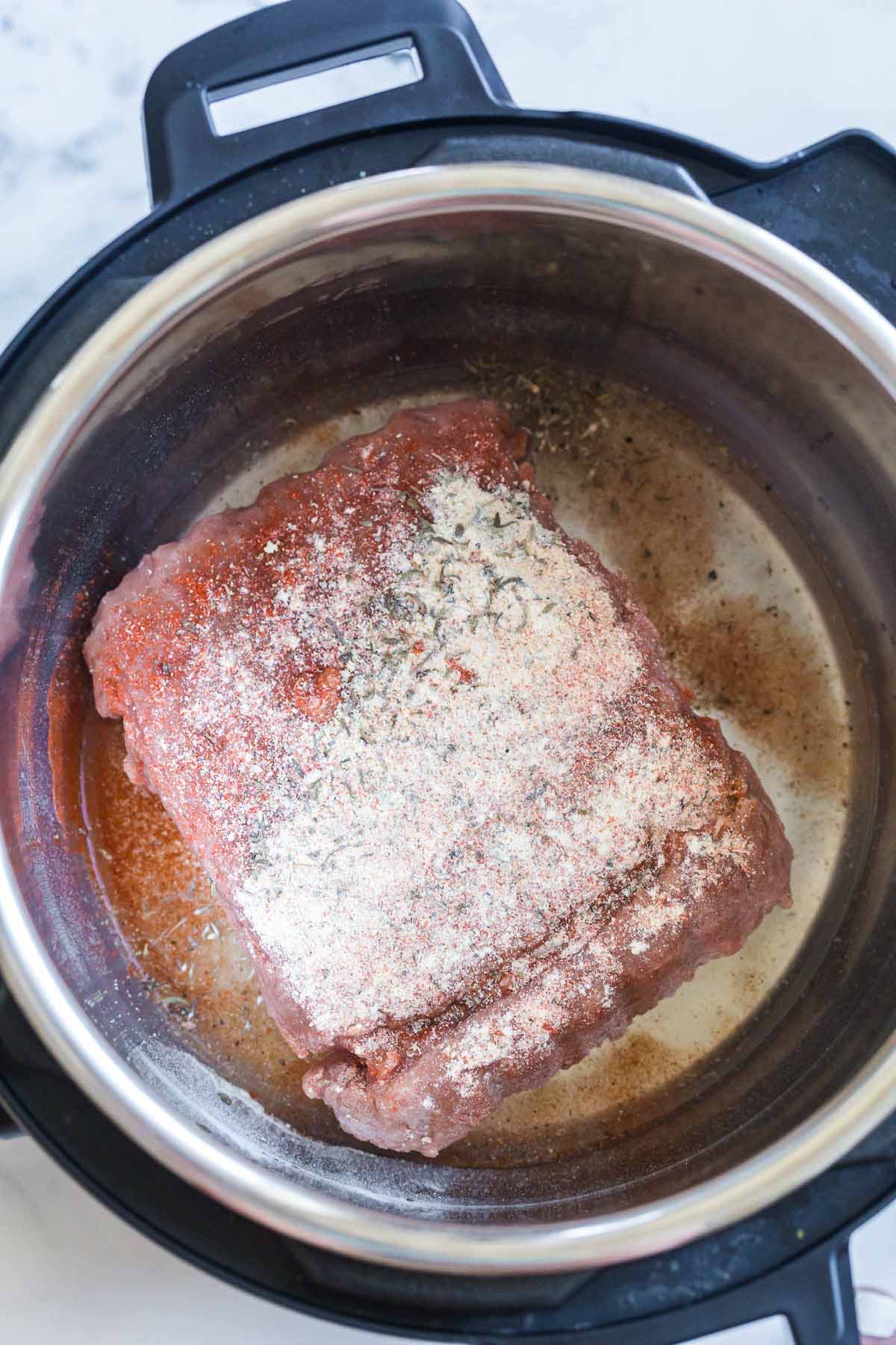 water and frozen ground turkey with seasonings on top inside of an instant pot.