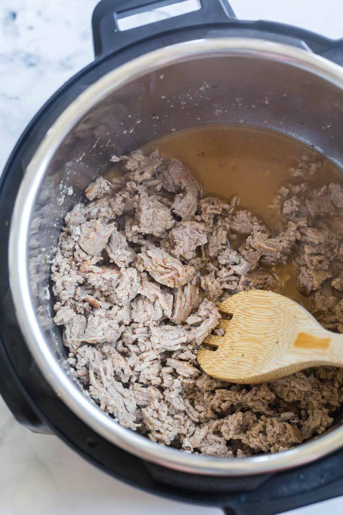 cooked ground turkey crumbled inside an instant pot being mixed with a wooded spoon.