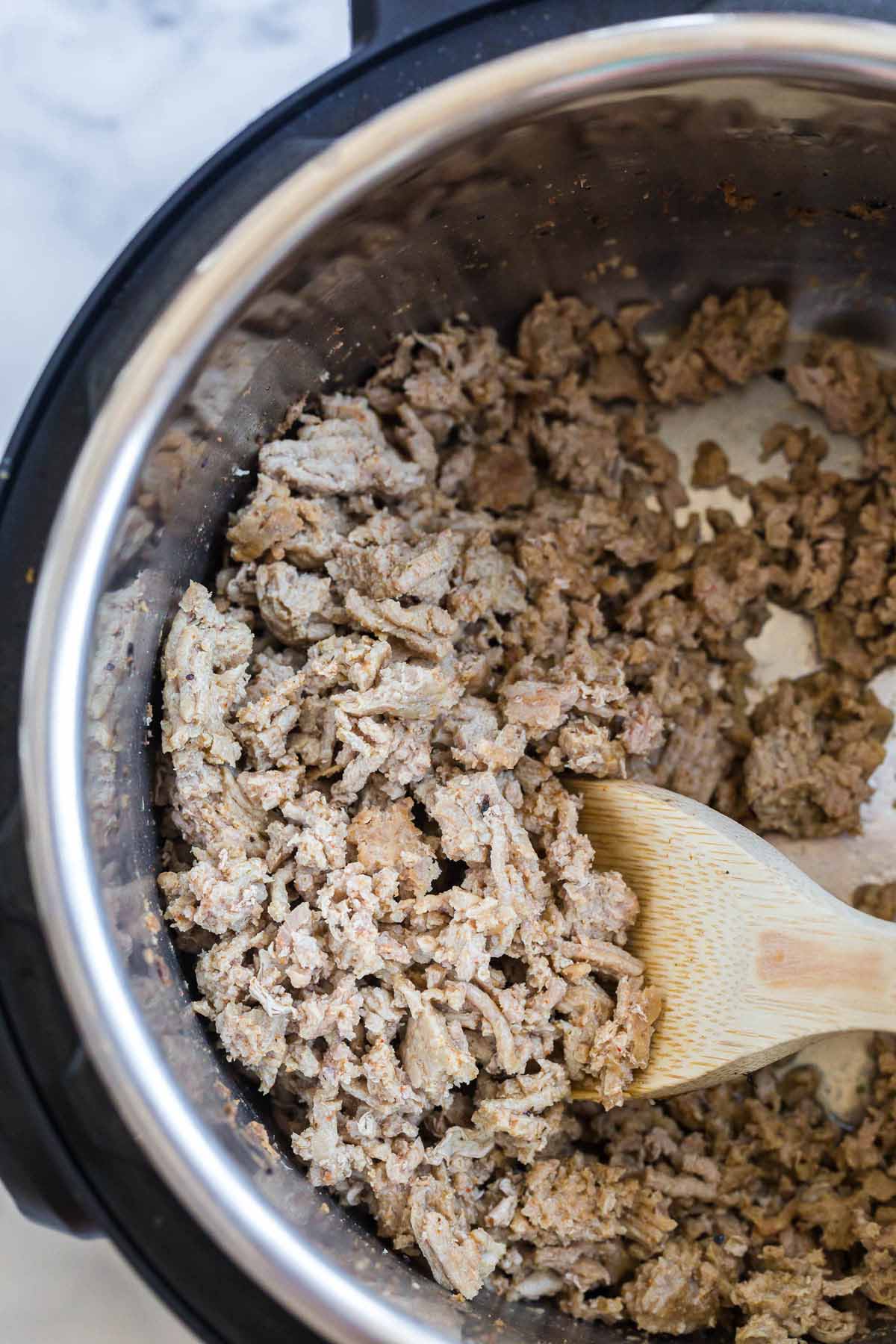 cooked ground turkey inside of an instant pot being mixed by a wooden spoon.