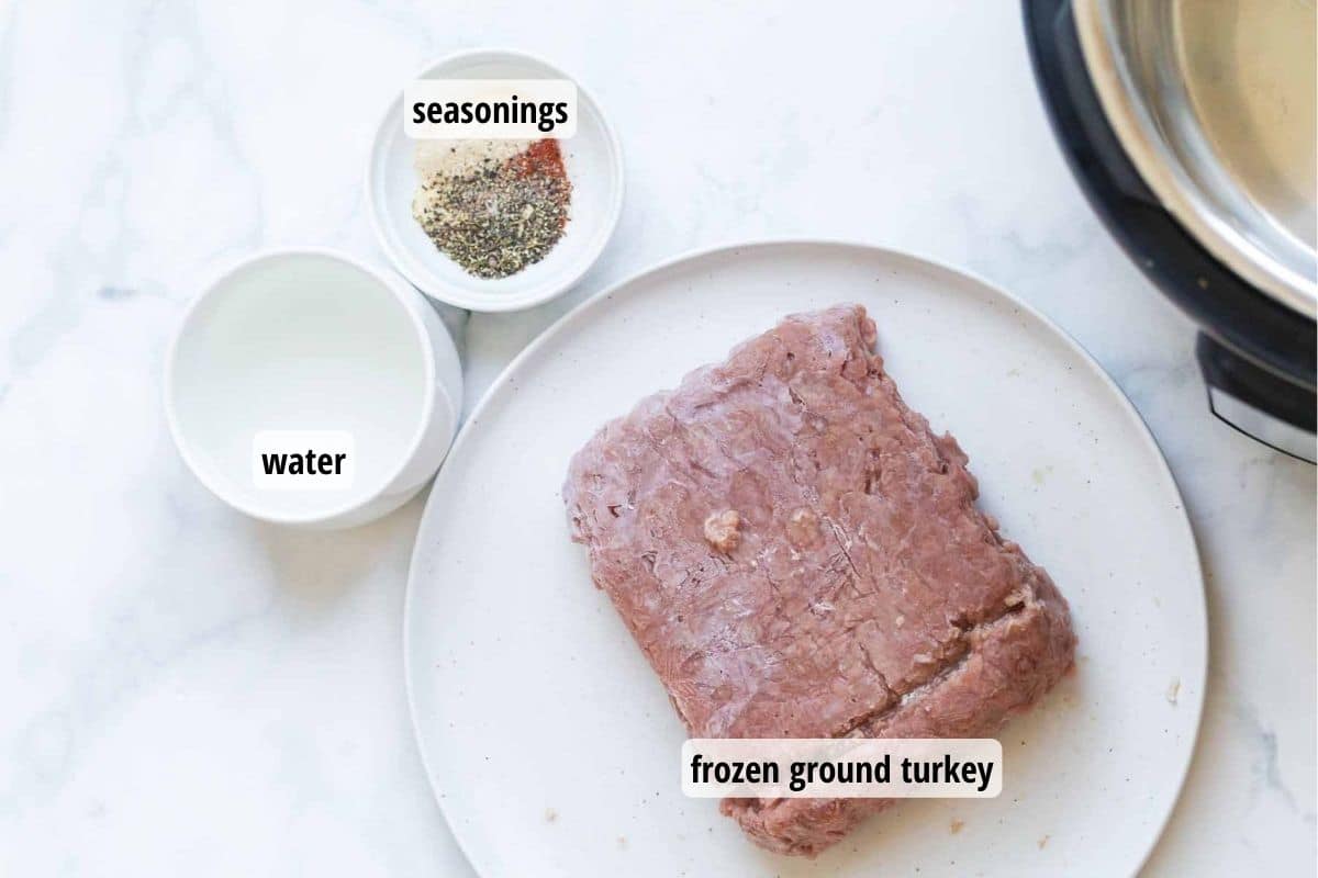 White counter with a plate topped with frozen ground turkey, and two bowls, one containing water and the other has a mixture of seasonings.
