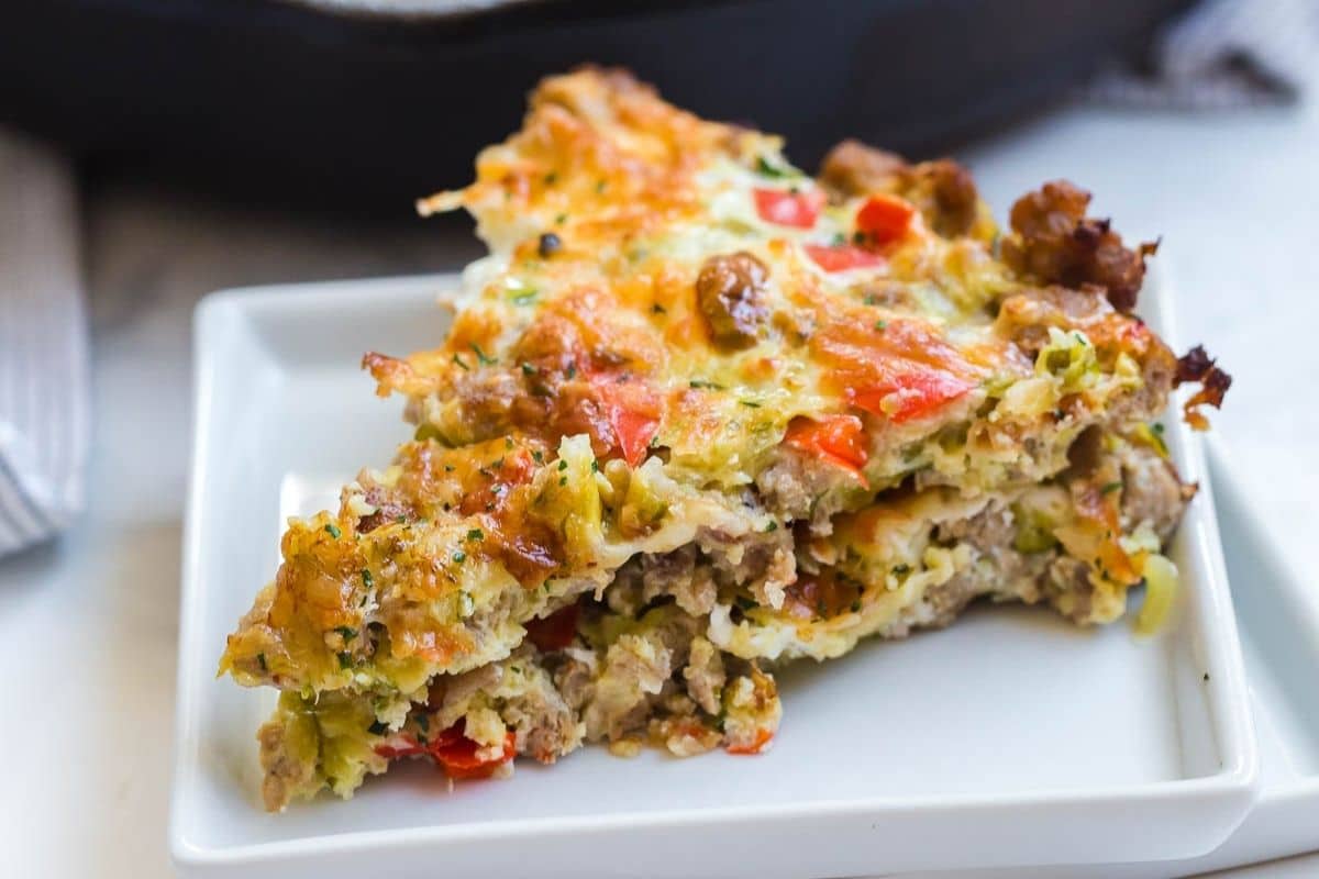 A white square plate with a slice of zucchini breakfast casserole on top.