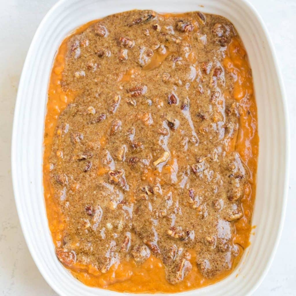 A white rectangular baking dish with mashed sweet potato casserole that has a sweet pecan topping and it is about to be baked.