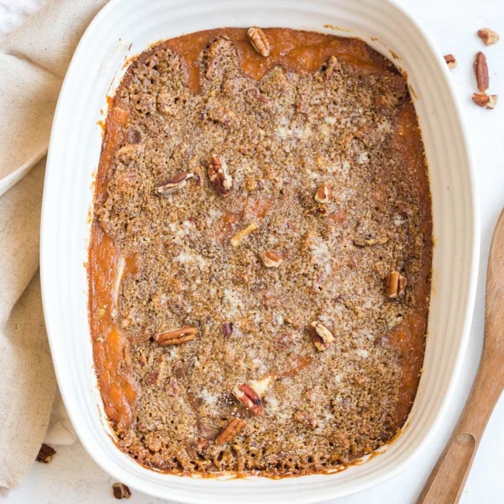 A white rectangular baking dish with mashed sweet potato casserole that has a crunchy pecan topping.