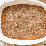 A white rectangular baking dish with mashed sweet potato casserole that has a crunchy pecan topping.