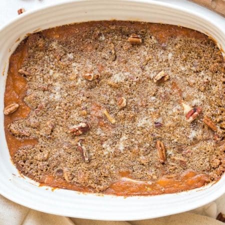 A white rectangular baking dish with mashed sweet potato casserole that has a crunchy pecan topping.