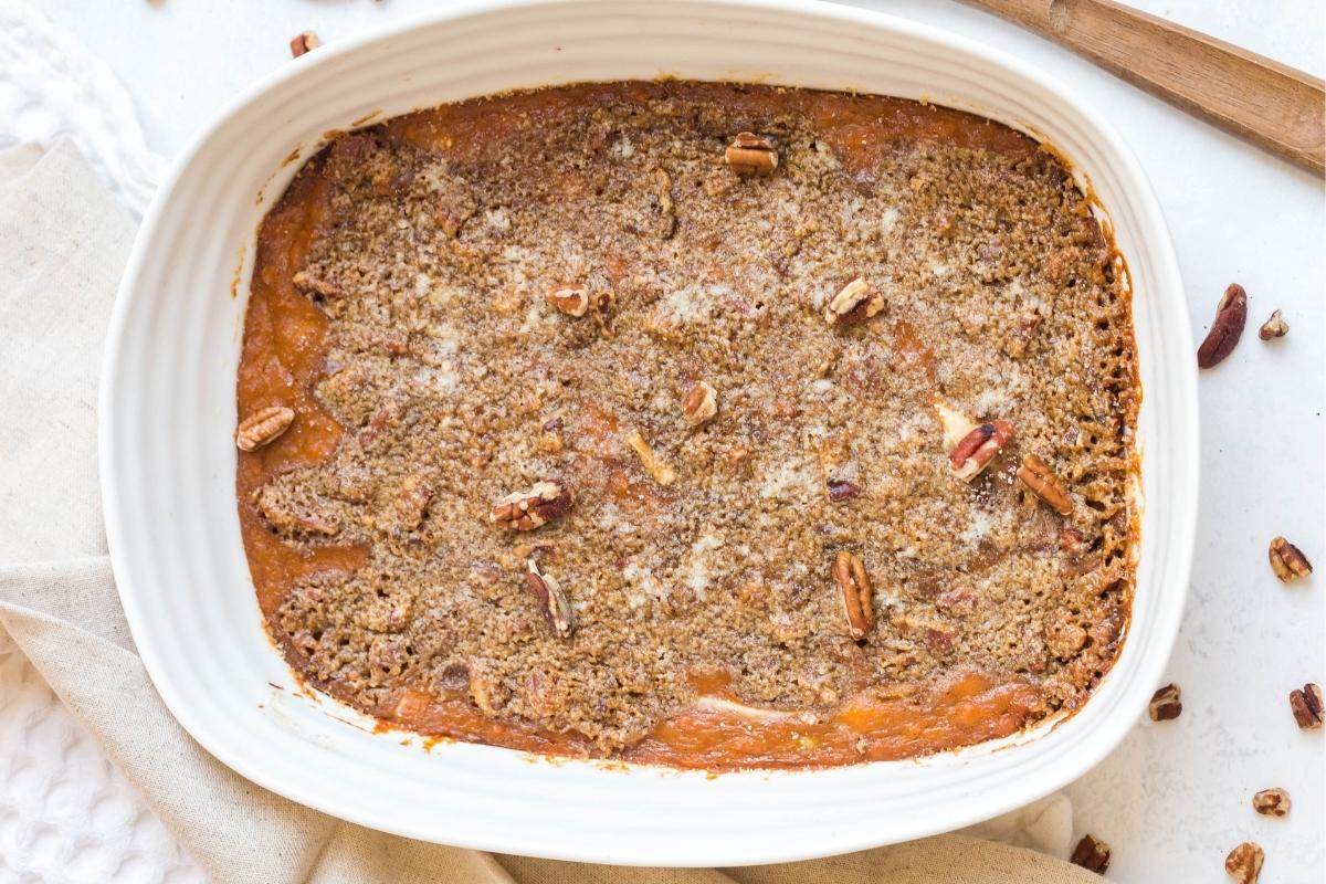 A white rectangular baking dish with mashed sweet potato casserole that has a crunchy pecan topping.