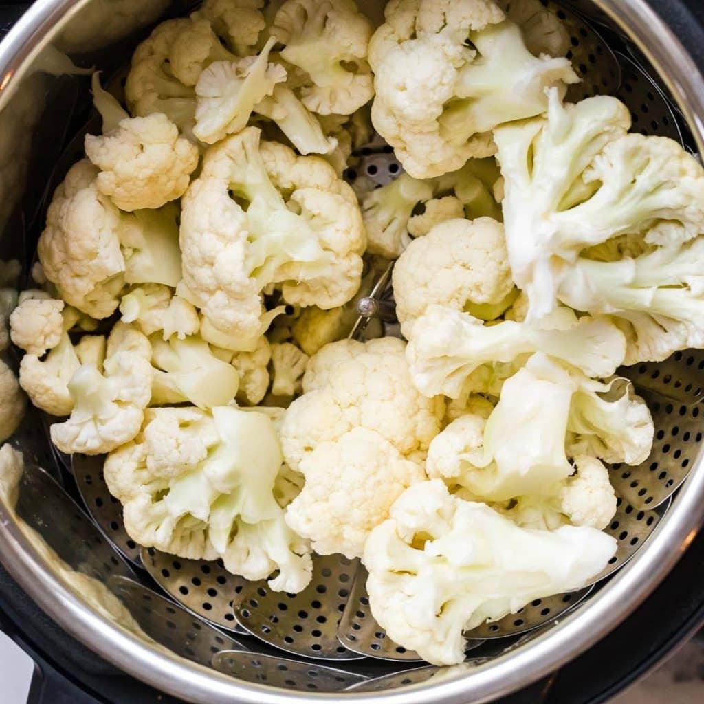 Chopped cauliflower sitting on a steamer basket inside an instant pot.