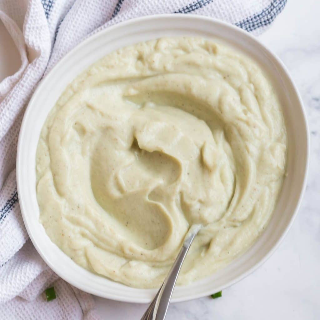 Mashed cauliflower inside of a white bowl which is sitting on a white linen napkin.