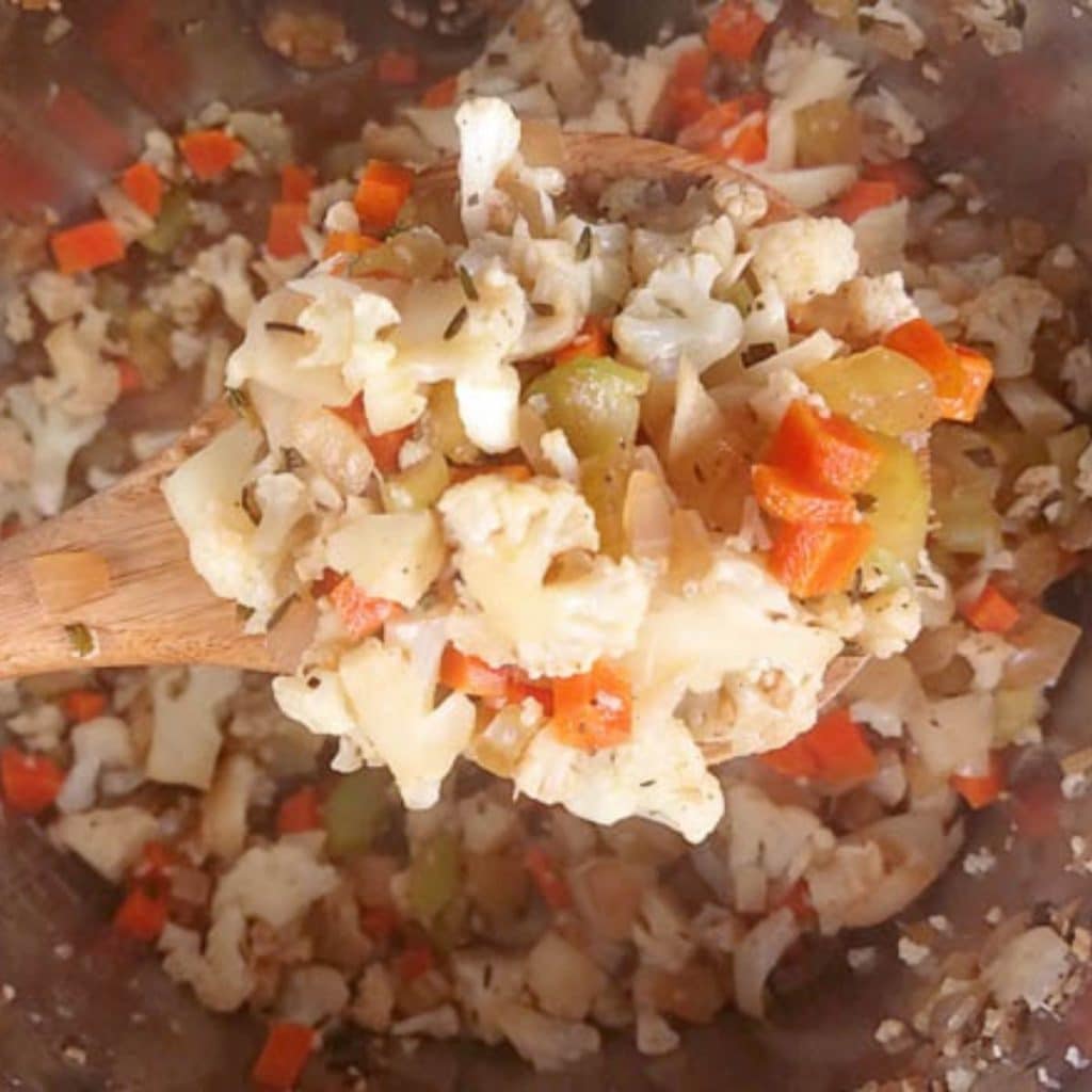 Cooked cauliflower stuffing being scooped out of an instant pot by a wooden spoon.