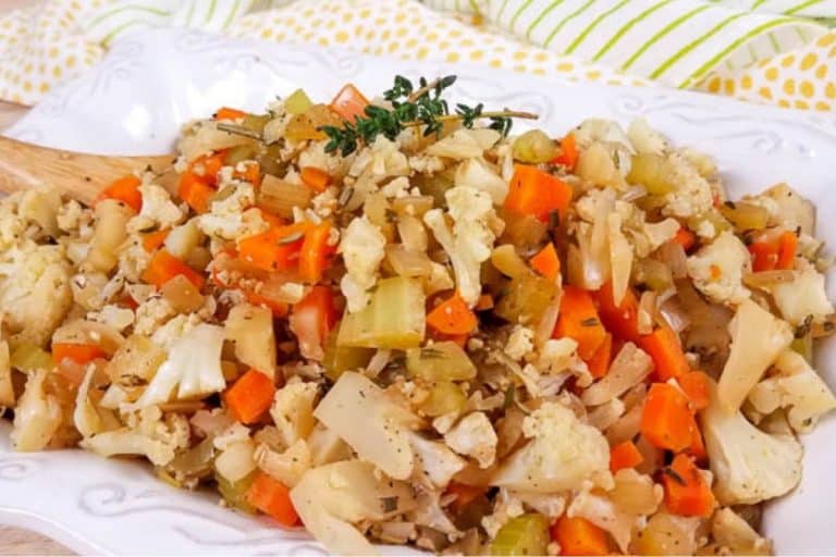 A white platter with cooked cauliflower stuffing with a sprig of thyme on top.