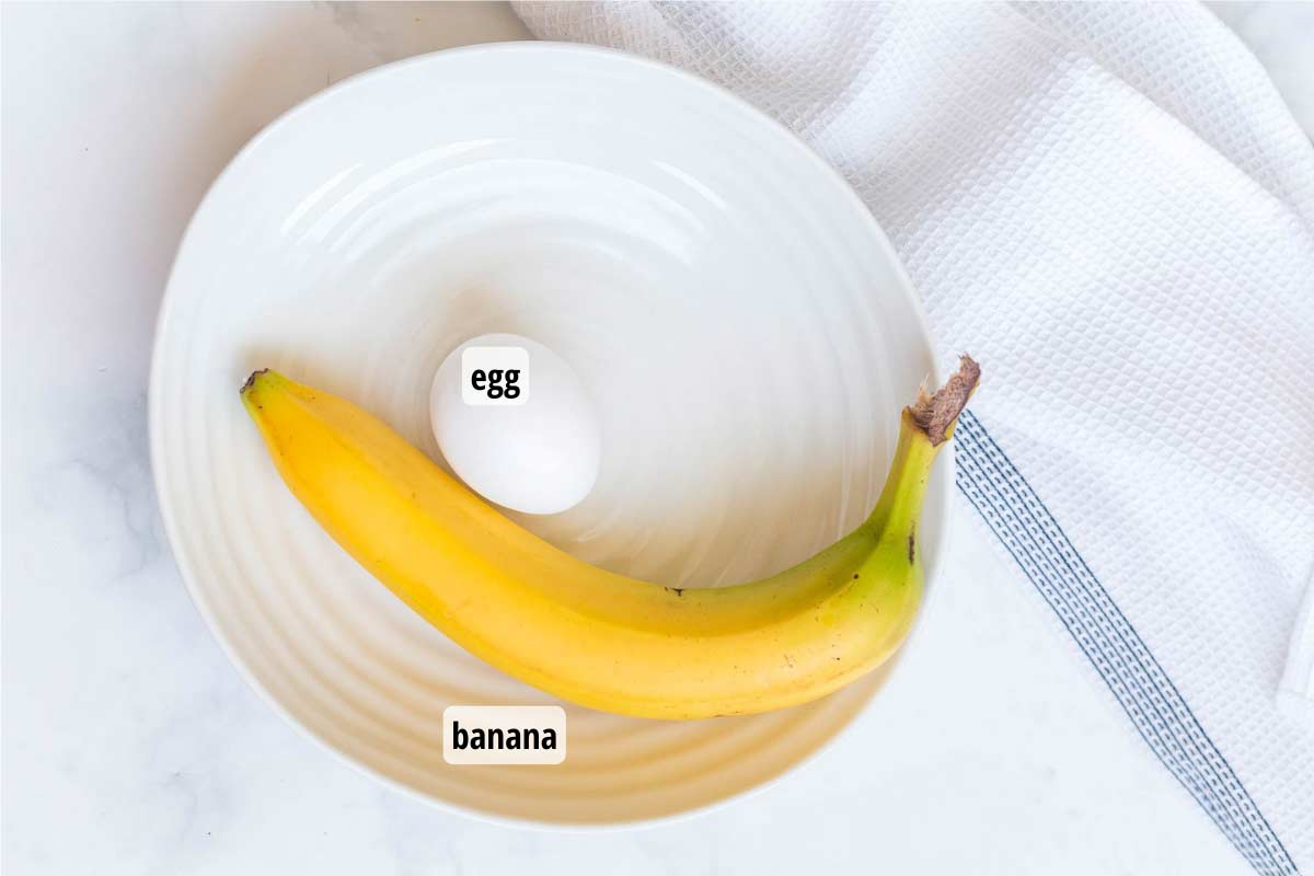White plate with an egg and a banana on it. There is a white towel with a blue stripe on the right of the plate.