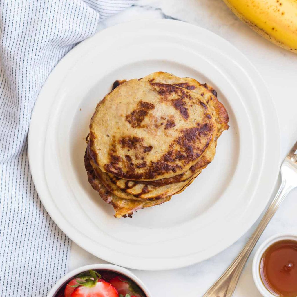 Cooked and browned banana pancakes in a stack on a white plate. 