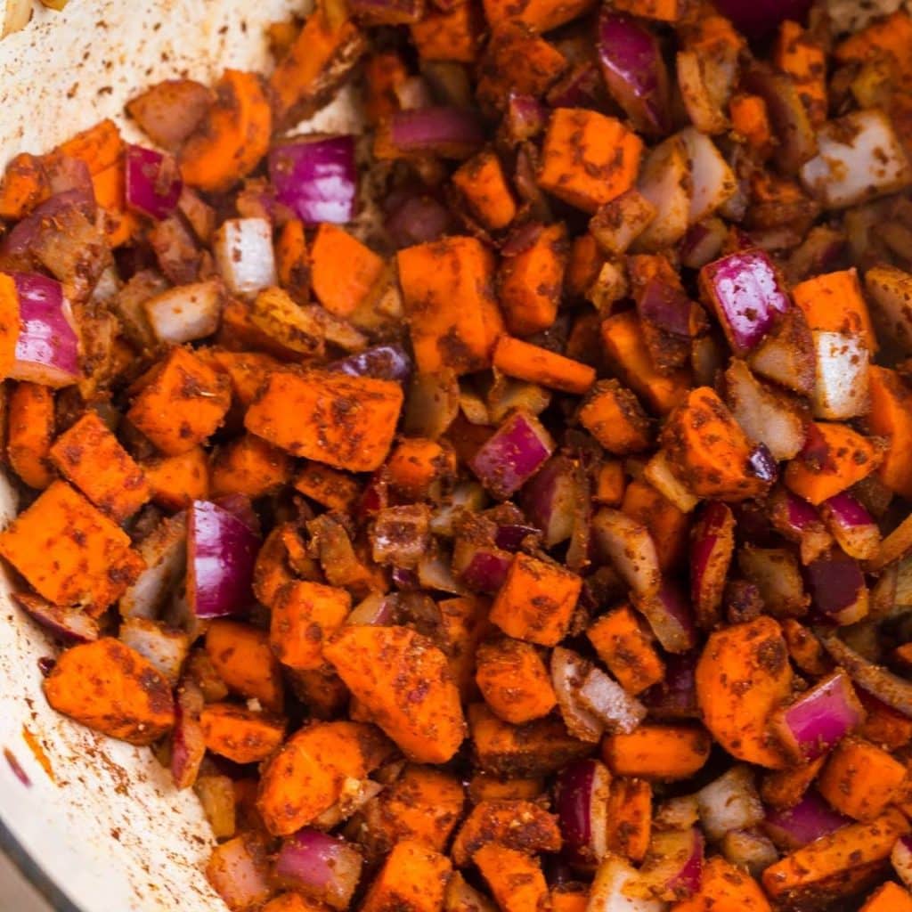 Diced carrots and onions being cooked inside of a pot with chili seasonings.