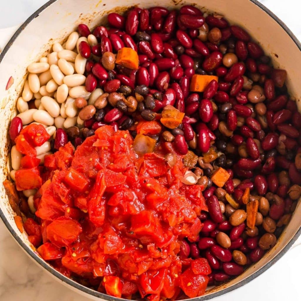 Four different types of beans, diced tomatoes, and diced carrots inside of a large pot being cooked to make chili.