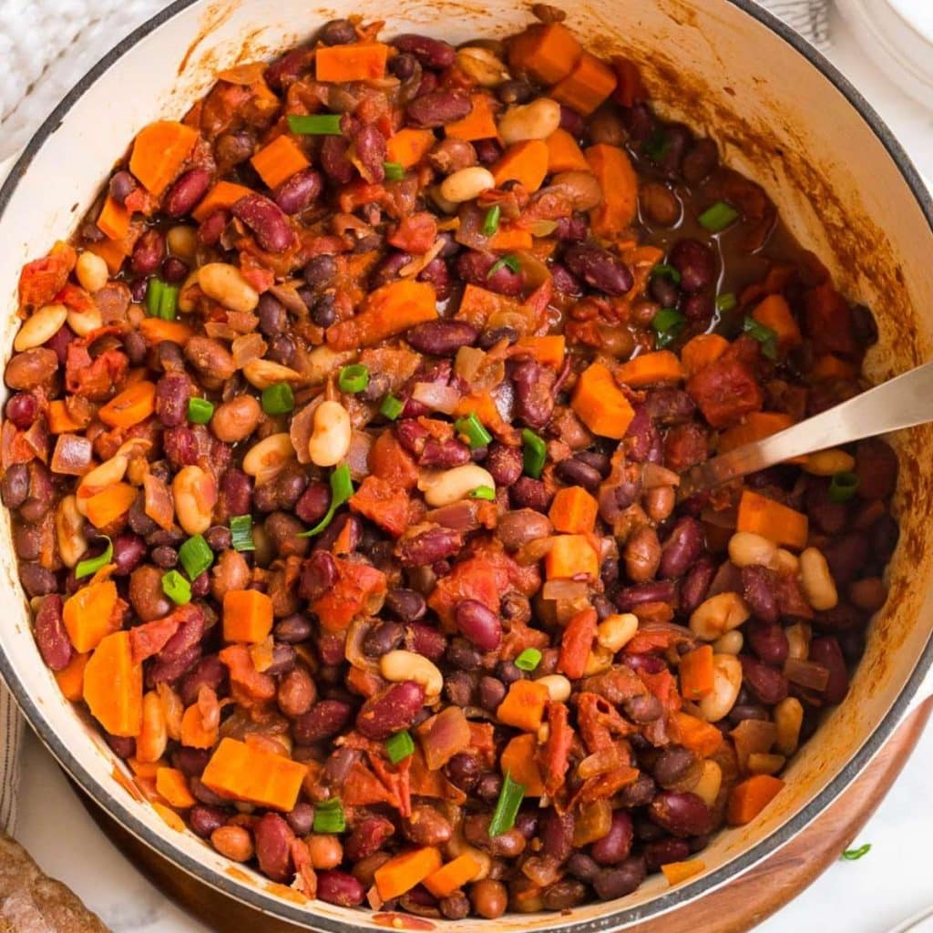 A large enameled pot with vegan chili being stirred with a spoon.