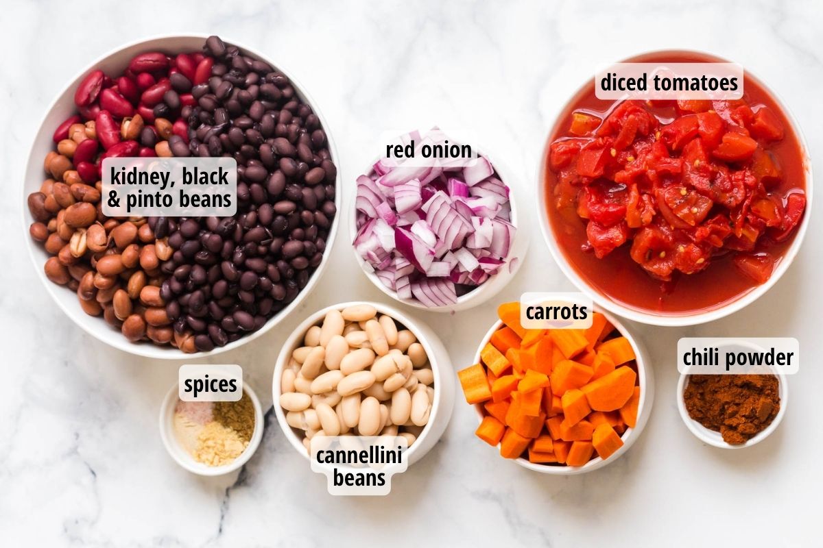 A white marbled counter top with 6 bowls of labeled ingredients needed to make the best vegan chili recipe.