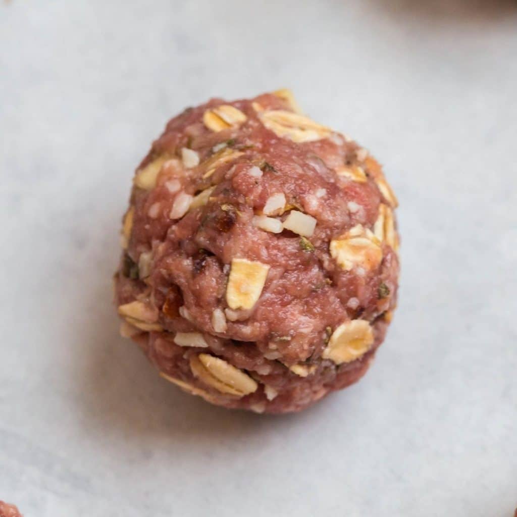 A single raw meatball sitting on top of parchment paper.