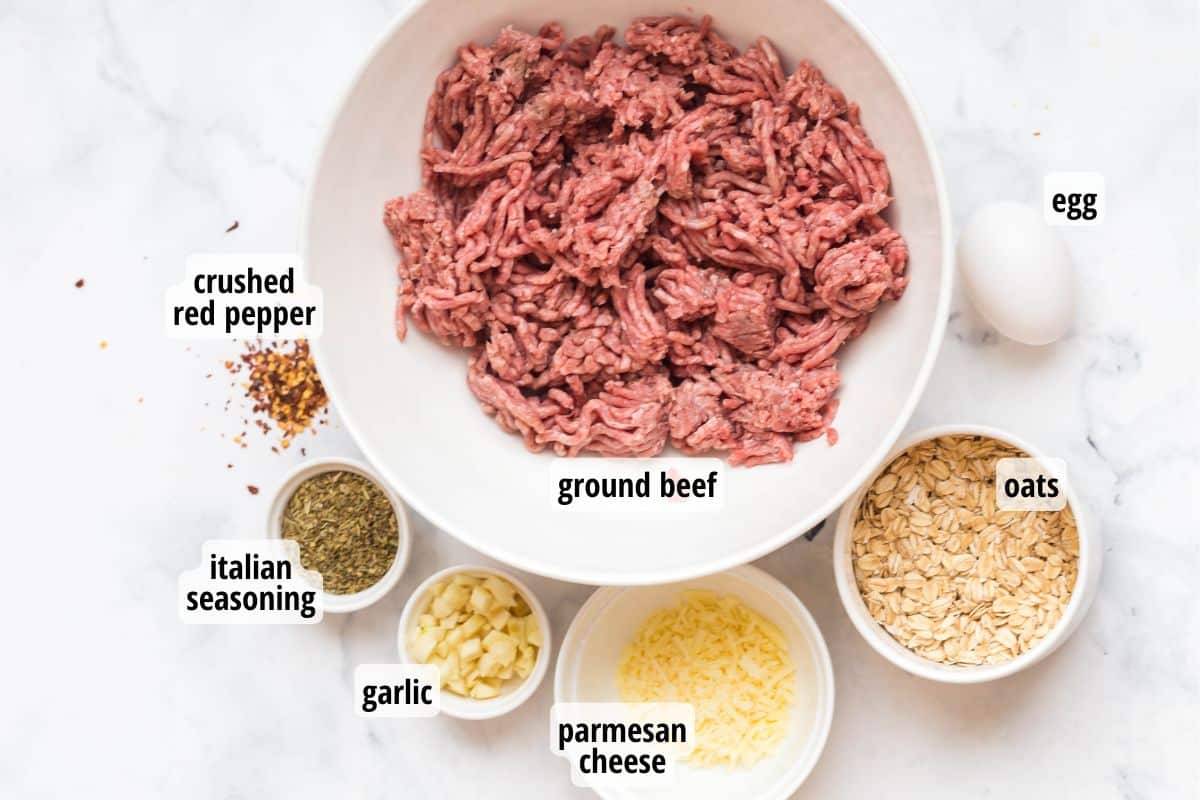 A white marbled counter top with labeled meatball ingredients in white bowls.
