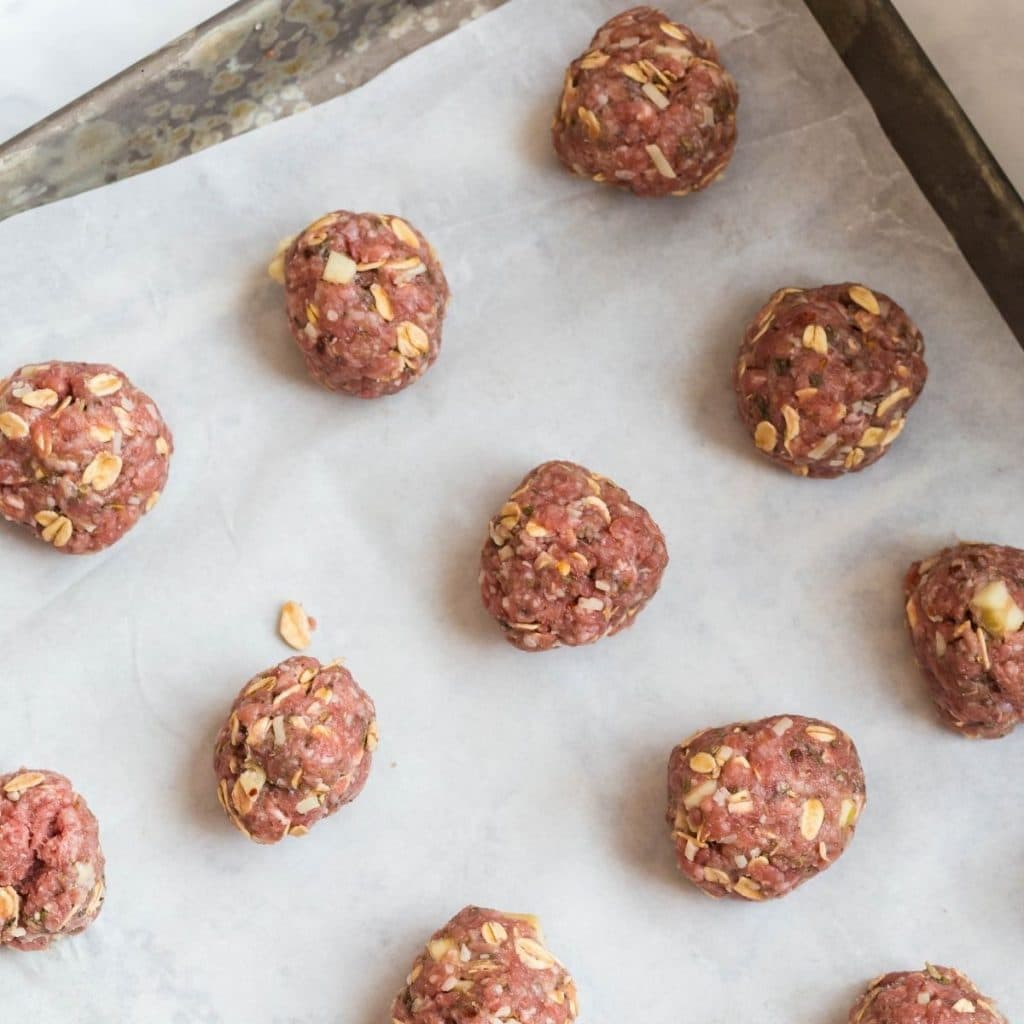 A parchment lined baking sheet with rolled raw meatballs.