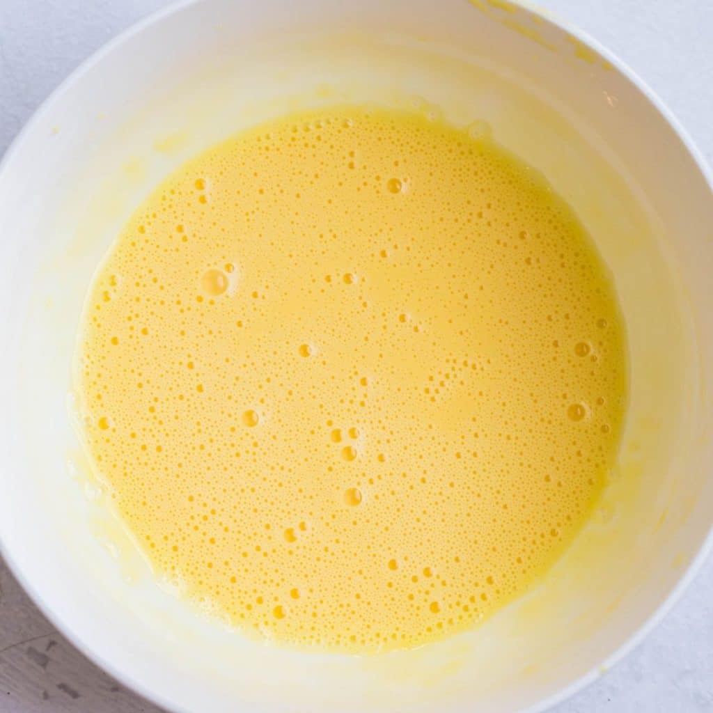 A white bowl with whisked together egg yolks and greek yogurt.