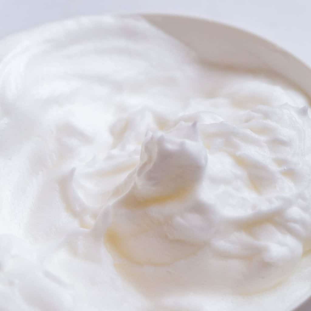 A white bowl with egg whites and baking soda that have been whisked together to form stiff peaks.